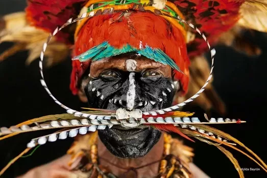 A Chimbu tribe chief’s face is painted with charcoal and crushed seashells. Bird of paradise feathers adorn his headdress and nose piercing.